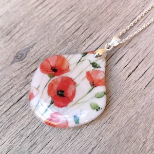 May include: A silver chain necklace with a teardrop-shaped pendant featuring a watercolor design of red poppies on a white background.