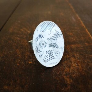 May include: A white oval ring with a delicate lace design.