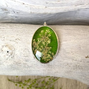 Oval pendant in green resin with white wild flowers inserted. H3.2xL2.2 cm. Thin stainless steel chain.