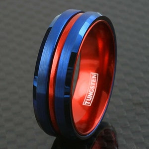 May include: A blue and red tungsten ring with a beveled edge and a brushed finish. The ring has a red stripe down the center and the word "TUNGSTEN" is engraved on the inside of the ring.