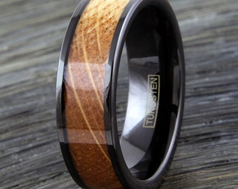 May include: A black tungsten ring with a brown wood inlay. The ring has a black band with a thin black line around the edge of the wood inlay. The ring is engraved with the word "TUNGSTEN".