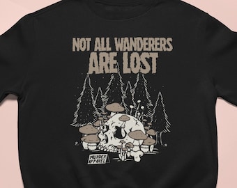 Puede incluir: Sudadera negra con un gráfico de una calavera rodeada de setas en un bosque. El texto "Not all wanderers are lost" está por encima del gráfico y "Murder Apparel" está por debajo del gráfico.
