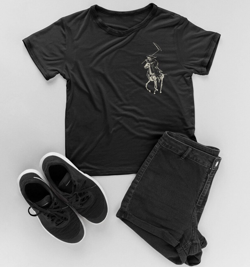 May include: A black t-shirt featuring a graphic of a skeleton riding a horse holding a scythe. The shirt is styled with black denim shorts and black trainers.