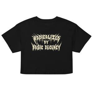 Pode incluir: Camiseta preta cropped com o texto "RADICALIZED BY BASIC DECENCY" em uma fonte gótica desgastada. A camiseta tem mangas curtas e gola redonda. O texto é em bege claro.