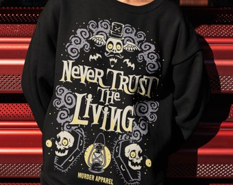 Puede incluir: Sudadera negra con un estampado gráfico de un esqueleto con un sombrero de copa y alas. El texto "Never Trust The Living" está impreso en amarillo en la parte delantera de la sudadera. El texto "Murder Apparel" está impreso en blanco en la parte inferior de la sudadera.