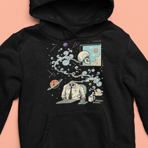 Könnte beinhalten: Schwarzer Hoodie mit einem Grafikdruck eines Skeletts mit einem Kopf in einer Wolke, einer Krawatte und einer Tastatur. Die Grafik ist von Sternen, Planeten und Wolken umgeben. Der Text "Murder Apparel" befindet sich am unteren Rand der Grafik.