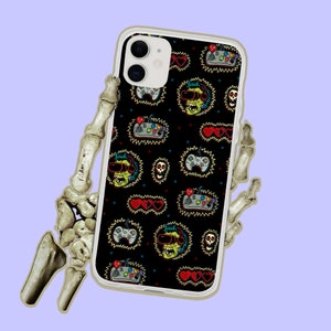 May include: A white phone case with a black background and a colorful pattern of video game controllers, skulls, hearts, and cartoon characters wearing VR headsets.