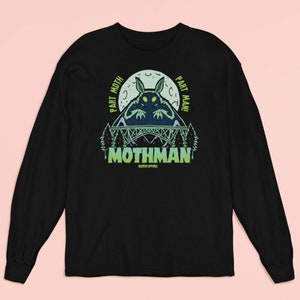 May include: Black long-sleeved t-shirt featuring a green and blue graphic of a mothman creature with the text "Part Moth, Part Man!" and "Mothman" below the creature.