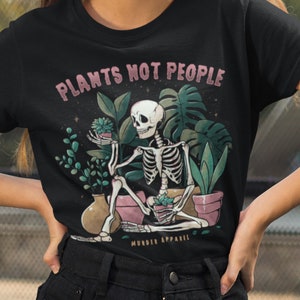 Könnte beinhalten: Schwarzes T-Shirt mit einem Grafikdruck eines Skeletts, das Topfpflanzen hält. Der Text "Plants Not People" befindet sich über dem Skelett und "Murder Apparel" darunter.
