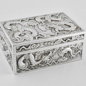 May include: A silver box with intricate dragon designs embossed on the lid and sides. The box is rectangular and has a hinged lid.