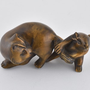 Puede incluir: Una detallada escultura de bronce de dos ardillas interactuando. Una ardilla está arqueada, mientras que la otra está de pie, con su pata tocando a la otra. La escultura tiene un acabado liso y pulido.