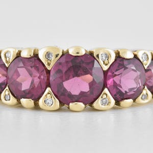May include: A gold and silver ring featuring five round, deep pink gemstones. Each gemstone is set in a gold bezel and accented with small diamonds. The ring has a classic, elegant design.