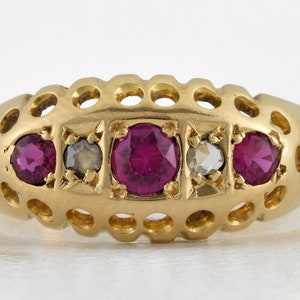 May include: A gold ring with a delicate openwork design and five gemstones. The ring features three round red rubies and two smaller round clear diamonds.