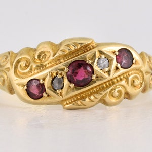 May include: A gold ring with a decorative design and three red gemstones and one clear gemstone.