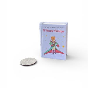 以下が含まれることがあります： 黒い持ち手と太字の黒い文字で「But First, Coffee」と書かれた白いセラミックマグ。マグカップはぼやけた背景に置かれています。マグカップの高さは約10cmです。