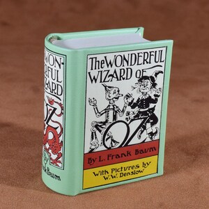 May include: A small, mint green book titled "The Wonderful Wizard of Oz" by L. Frank Baum. The cover features illustrations of the Tin Man and the Scarecrow. The spine displays the title and a red dragon illustration.