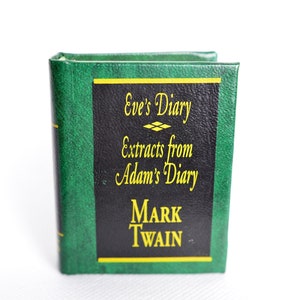May include: A small, hardcover book titled "Eve's Diary Extracts from Adam's Diary" by Mark Twain. The book has a green cover with a black panel featuring yellow text. The book is standing upright against a white background.