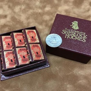 Puede incluir: Un conjunto de libros en miniatura de Sherlock Holmes en una caja de color burdeos. La caja tiene letras doradas que dicen "The Complete Sherlock Holmes".