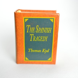 Può includere: Un piccolo libro di colore marrone-arancione con dorso verde e lettere dorate. Il titolo è "The Spanish Tragedy" di Thomas Kyd.