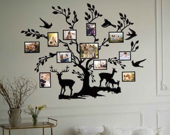 May include: Black silhouette of a tree with deer and birds, with multiple photo frames hanging on the branches. The tree is mounted on a white wall in a room with a bed and a side table.