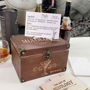 May include: A wooden box with a hinged lid and a brass latch. The box is engraved with the words "Mixology" and "Michael". There is a small card with a recipe for a Mojito drink.
