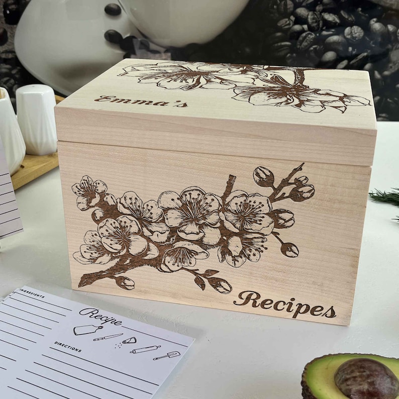 K&ouml;nnte beinhalten: Eine Holzkisten f&uuml;r Rezepte mit einem Blumendesign und dem Wort "Rezepte" auf der Vorderseite. Die Kiste ist mit dem Namen "Emma's" personalisiert.