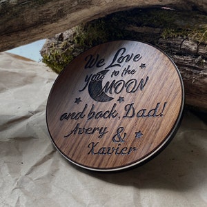 May include: A round wooden sign with the text "We Love You to the Moon and back, Dad! Avery & Xavier" engraved on it. The sign features a crescent moon and stars.