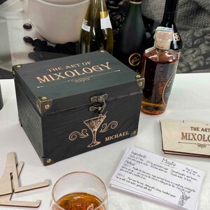 May include: A black wooden box with a brass latch and the words "The Art of Mixology" engraved on the lid. The box is personalised with the name "Michael". A recipe card for a Mojito cocktail is visible in the foreground.