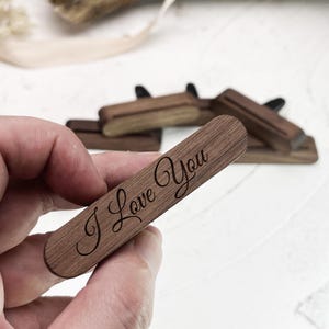 Puede incluir: Un ambientador de coche de madera con el texto "I Love You" grabado en una fuente cursiva.