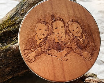 May include: A round wooden plaque with a silver rim, featuring an engraved image of three smiling children. The wood has a warm, reddish-brown hue. The image is detailed, showing the children's clothing and facial expressions.