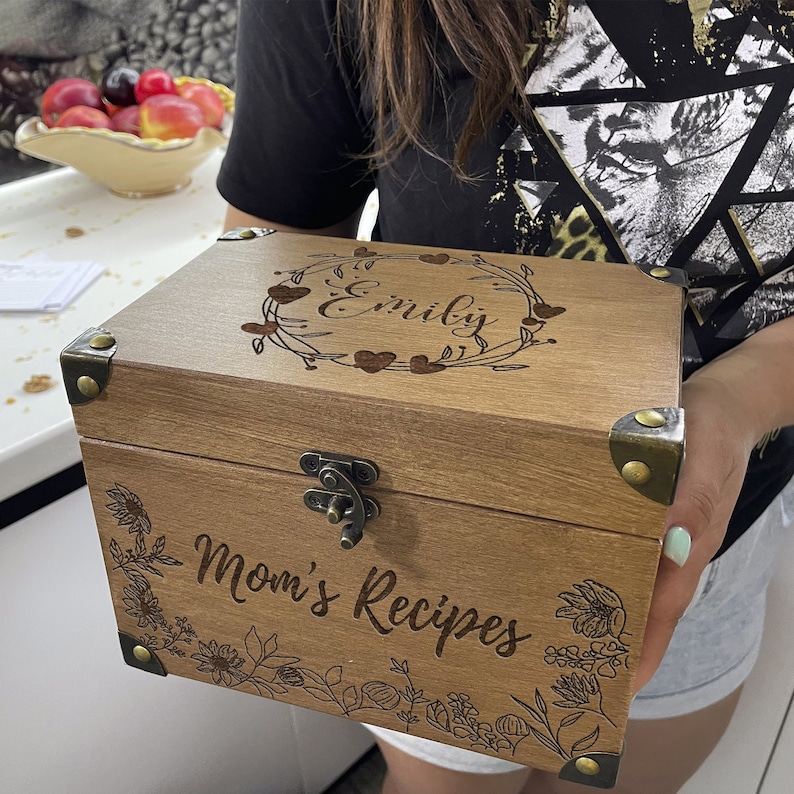 May include: A wooden box with a hinged lid and a latch. The box is engraved with the text "Emily's Mom's Recipes" and a floral design.