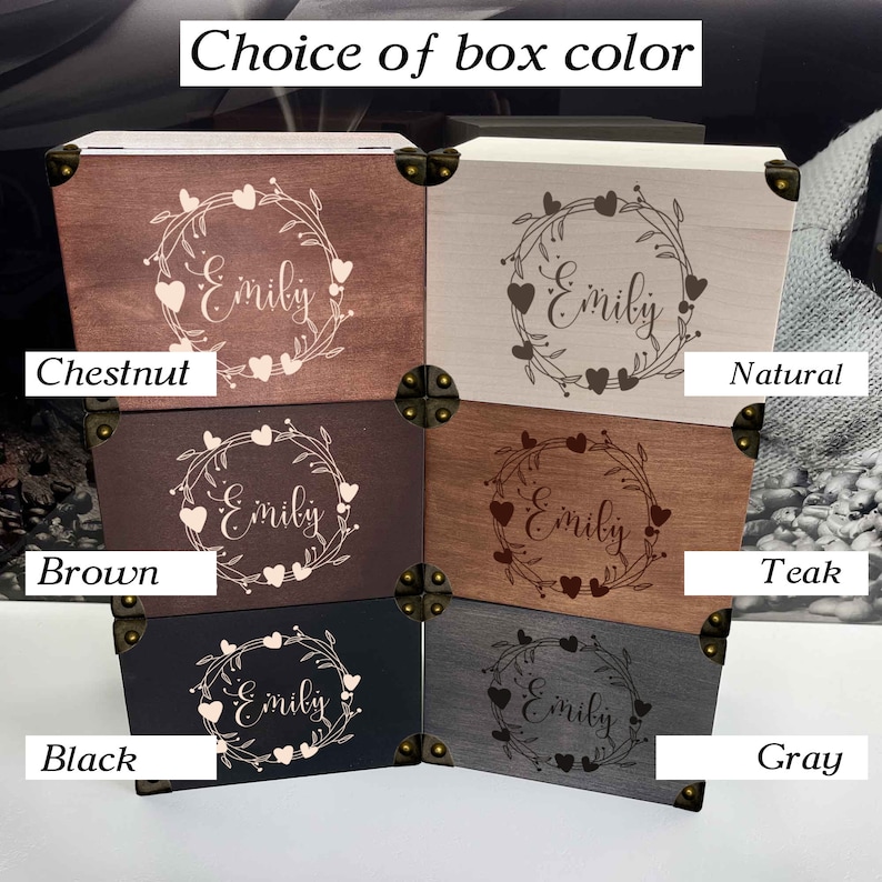 May include: Six wooden boxes with different wood finishes, each with a heart wreath design and the name "Emily" engraved on the lid. The boxes are labeled with the wood finishes: Chestnut, Natural, Teak, Brown, Gray, and Black.