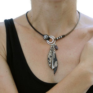Può includere: Un girocollo in pelle marrone con un ciondolo circolare in argento e un pendente di piume di pelle marrone e bianco.