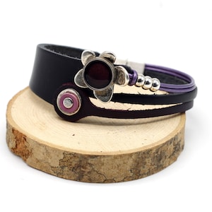 May include: A black leather bracelet with a purple leather strap and a silver flower charm with a dark purple stone in the center.