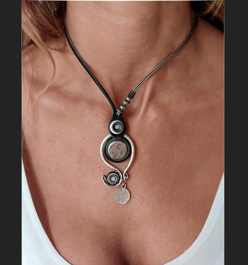 Pu&ograve; includere: Una collana argento e nera con un ciondolo unico che presenta un cerchio con un cerchio pi&ugrave; piccolo all'interno, un cerchio testurizzato e un cerchio pendente. La collana &egrave; realizzata in pelle e ha una catena argentata.