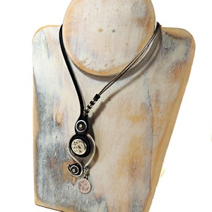 Pu&ograve; includere: Una collana in pelle nera con un ciondolo d'argento con un design a spirale e due accenti rotondi. Il ciondolo &egrave; appeso a una catena d'argento.