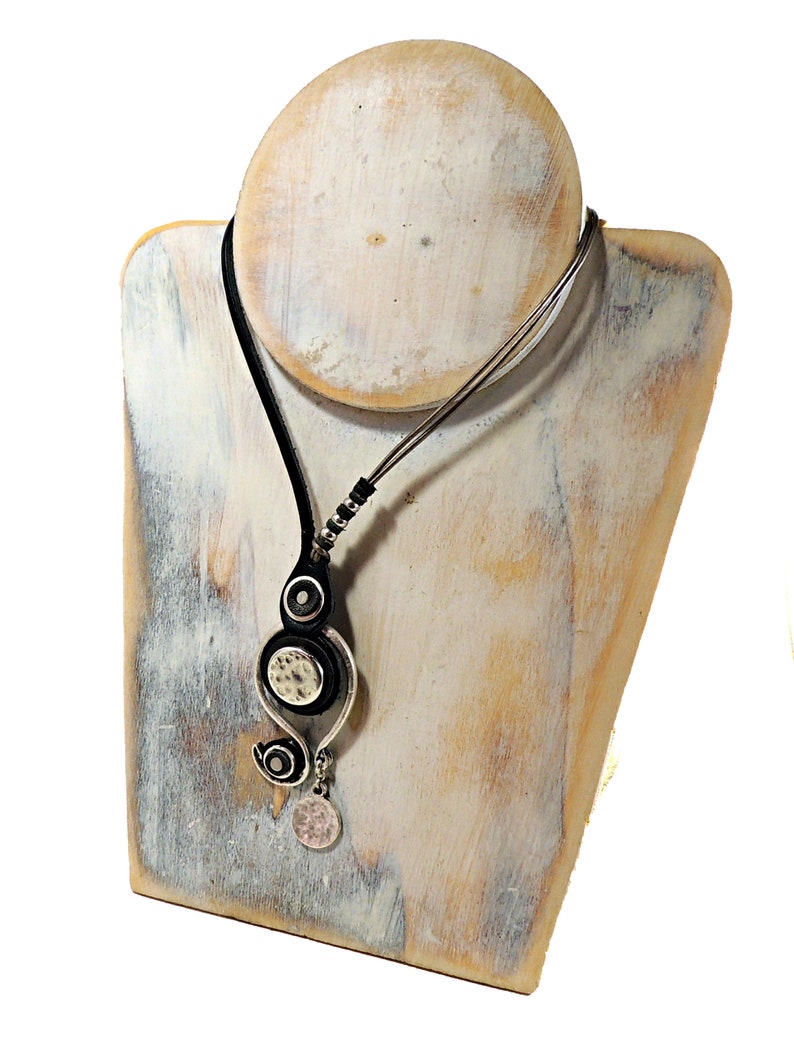 Pu&ograve; includere: Una collana in pelle nera con un ciondolo d'argento con un design a spirale e due accenti rotondi. Il ciondolo &egrave; appeso a una catena d'argento.