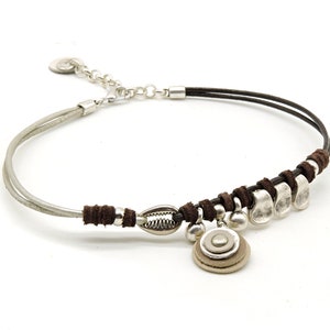 Op de afbeelding: Een bruine leren ketting met zilveren kralen en een zilveren hanger. De hanger is een cirkel met drie lagen en een kleine zilveren kraal in het midden.