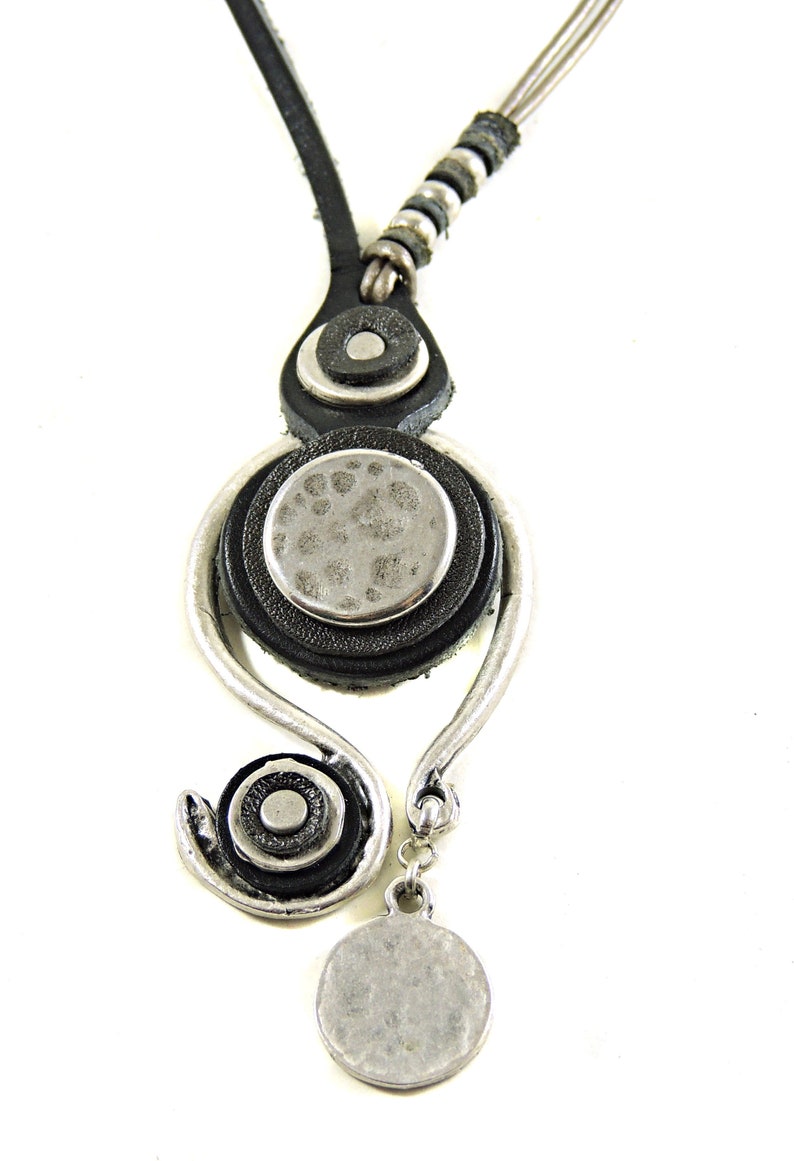 Pu&ograve; includere: Una collana in pelle nera con un ciondolo d'argento che presenta un cerchio con una superficie testurizzata e un cerchio pi&ugrave; piccolo con una superficie liscia. La collana ha una catena d'argento con un ciondolo rotondo d'argento.