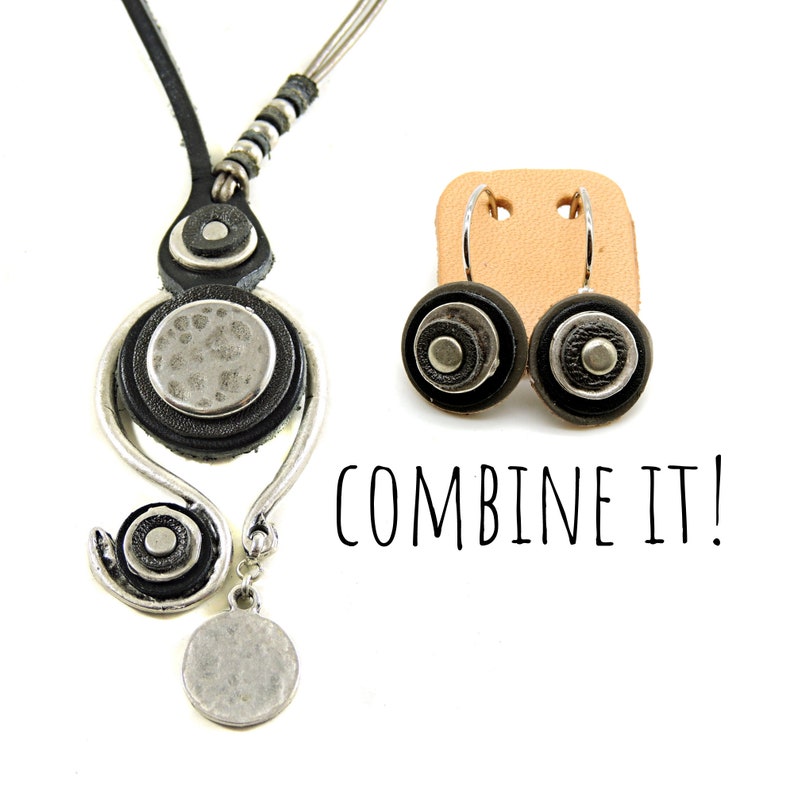 Pu&ograve; includere: Una collana in pelle nera con dettagli argentati e un paio di orecchini abbinati. La collana presenta un ciondolo rotondo con una finitura argentata martellata e gli orecchini hanno un design simile. Il testo "COMBINE IT!" &egrave; scritto sotto gli orecchini.