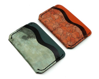 May include: Two leather card holders with a wavy design. One is green with black accents and the other is orange with brown accents.