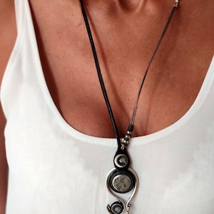 Pu&ograve; includere: Una collana in argento e nero con un designo di ciondolo unico. Il ciondolo presenta tre elementi circolari, di cui due in argento e uno in nero. La collana &egrave; in pelle e ha una catena in argento.