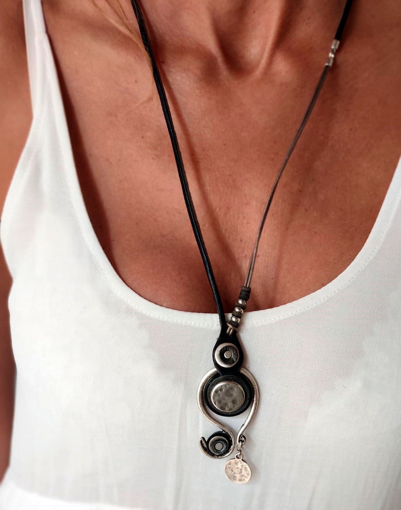 Pu&ograve; includere: Una collana in argento e nero con un designo di ciondolo unico. Il ciondolo presenta tre elementi circolari, di cui due in argento e uno in nero. La collana &egrave; in pelle e ha una catena in argento.