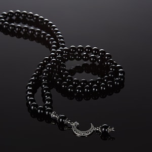 May include: A black prayer bead necklace with a crescent moon charm. The beads are made of black onyx and the charm is made of silver.