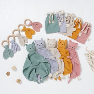 Pode incluir: Conjunto de cinco brinquedos para bebés em forma de gato, com textura macia de gaze. Cada brinquedo tem uma cor diferente e vem com uma bolsa de cordão combinando. Os brinquedos são perfeitos para aconchegar e acalmar os bebés.