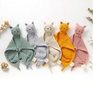 May include: Five soft, plush cat-shaped baby security blankets in different colors: green, gray, beige, yellow, and pink. Each blanket has a knotted tail and a cute embroidered face.