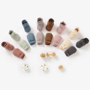 May include: A collection of 12 pairs of baby booties in various colors, including brown, gray, beige, and blue. The booties are made of a soft, ribbed fabric and have a button closure.