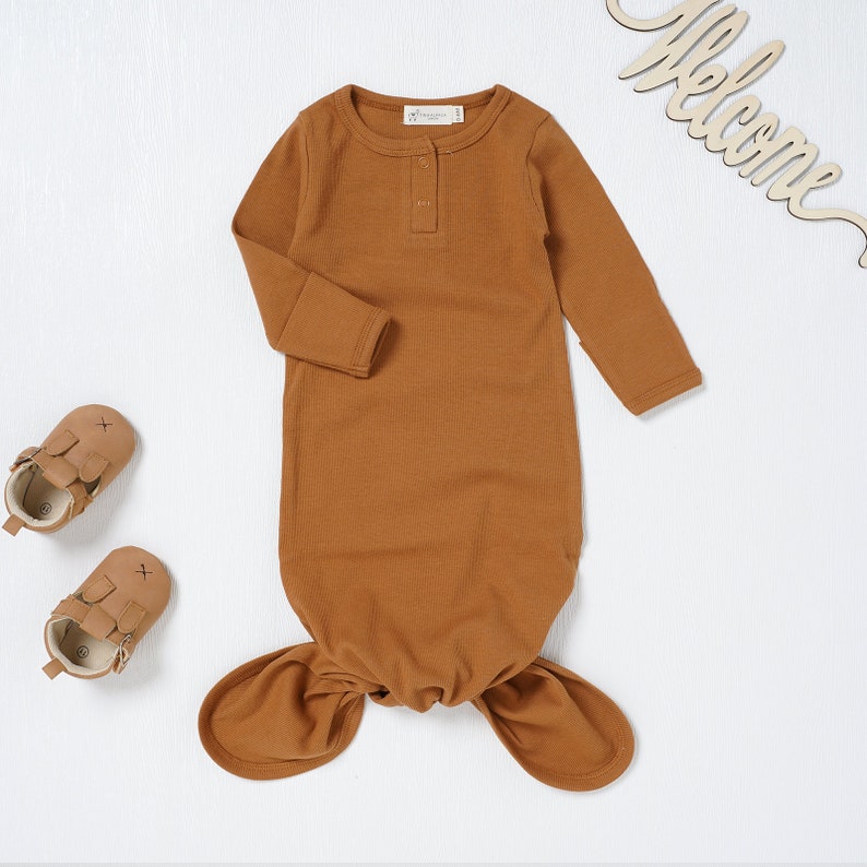 May include: A brown long-sleeved knotted baby gown with a single button closure at the neckline.
