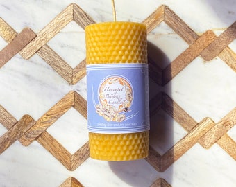 Op de afbeelding: Een gele bijenwaskaars met een honingraatpatroon. De kaars heeft een blauw etiket met de tekst "Honeycomb Beeswax Candles" en "Sending love and joy your way".