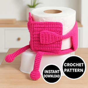 Op de afbeelding: Een rol wit toiletpapier is verpakt in een felroze gehaakte hoes. De hoes heeft een vierkant lichaam met armen en benen en een klein klepje. De woorden "Instant Download" en "Crochet Pattern" staan in zwarte cirkels.